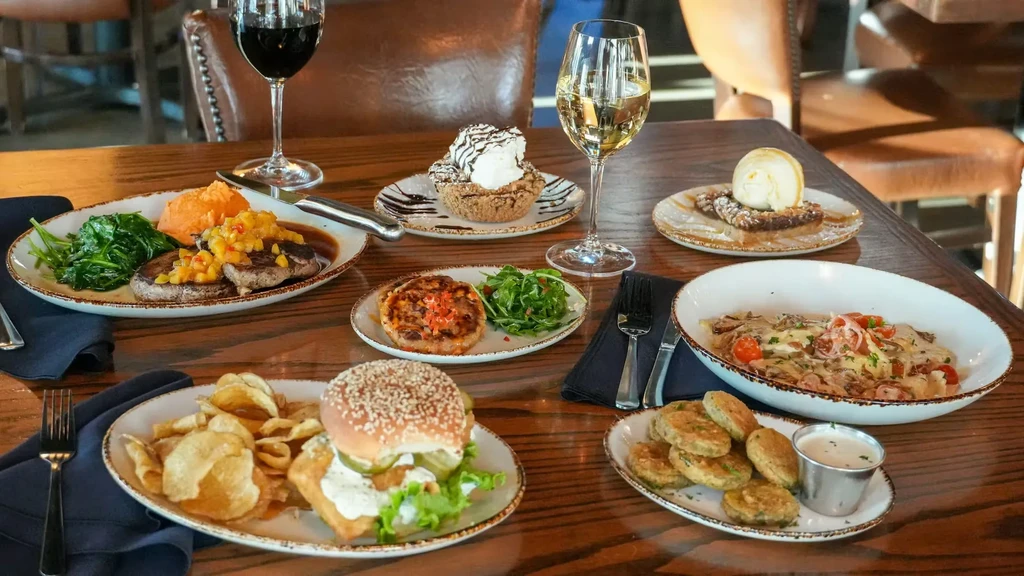 Various restaurant dishes, desserts, and wine spread on a wooden table.
