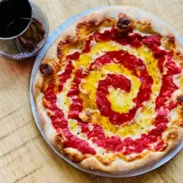 Freshly baked pizza with spiral cheese, wine on a rustic table.