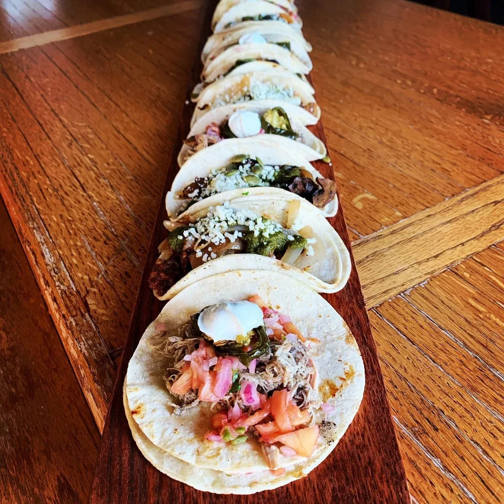 Meticulously arranged tacos with diverse fillings on a wooden board.