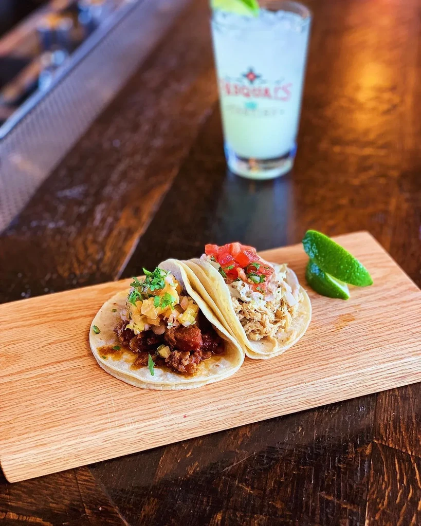 Two tacos with pineapple salsa and tomatoes, on a wooden board.