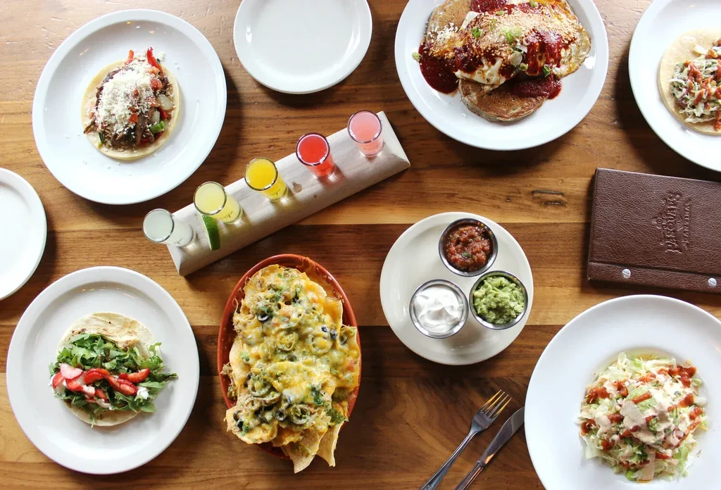 Overhead view of a wooden table with many Mexican dishes and colorful drinks.