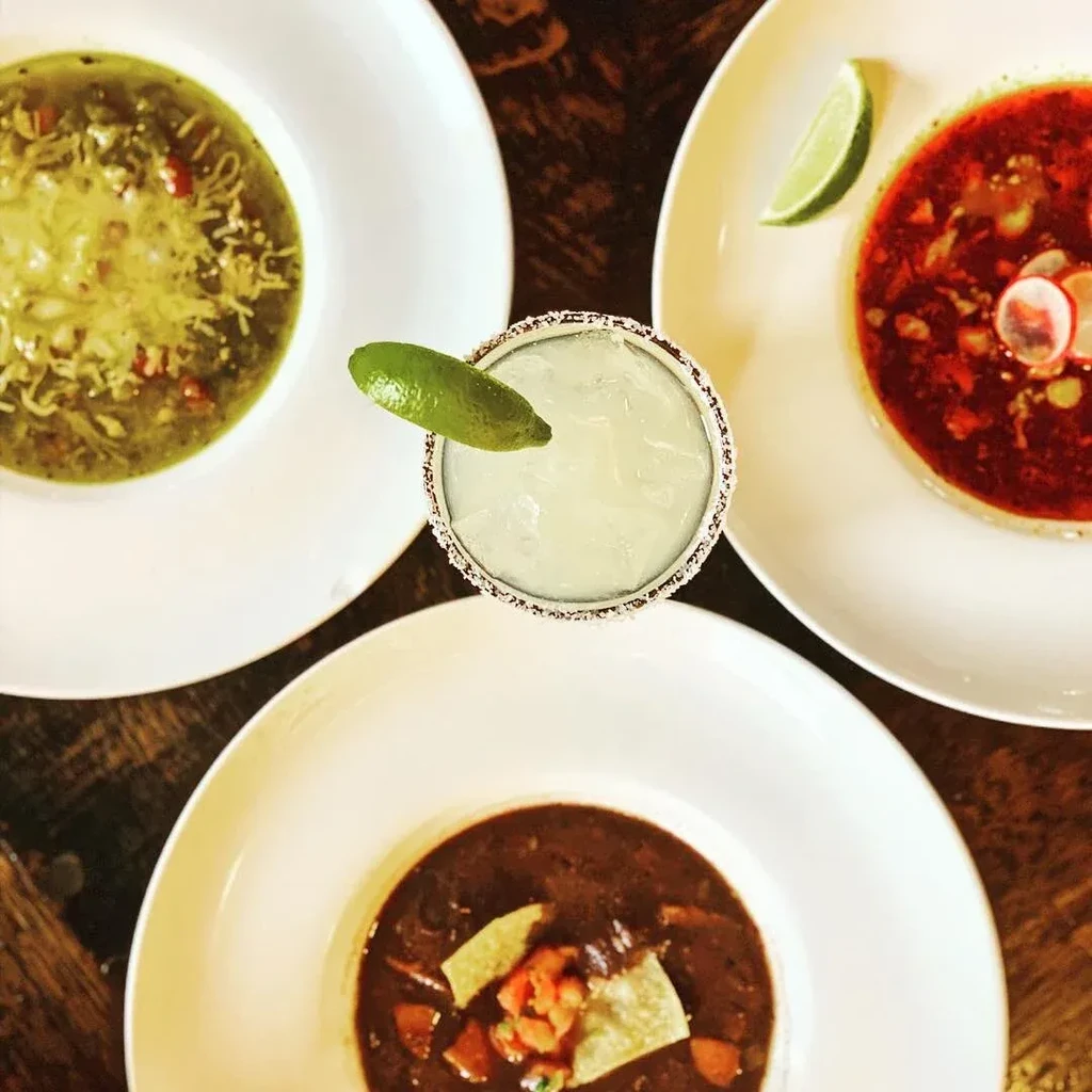 Overhead view of three different soups and a margarita on a table.