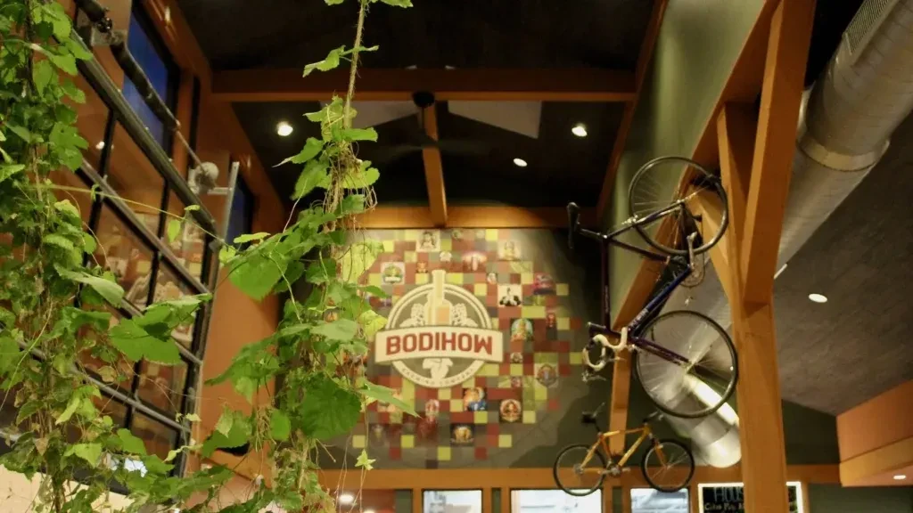 Restaurant interior with wooden beams, exposed ductwork, mounted bikes, BODIHOW logo.