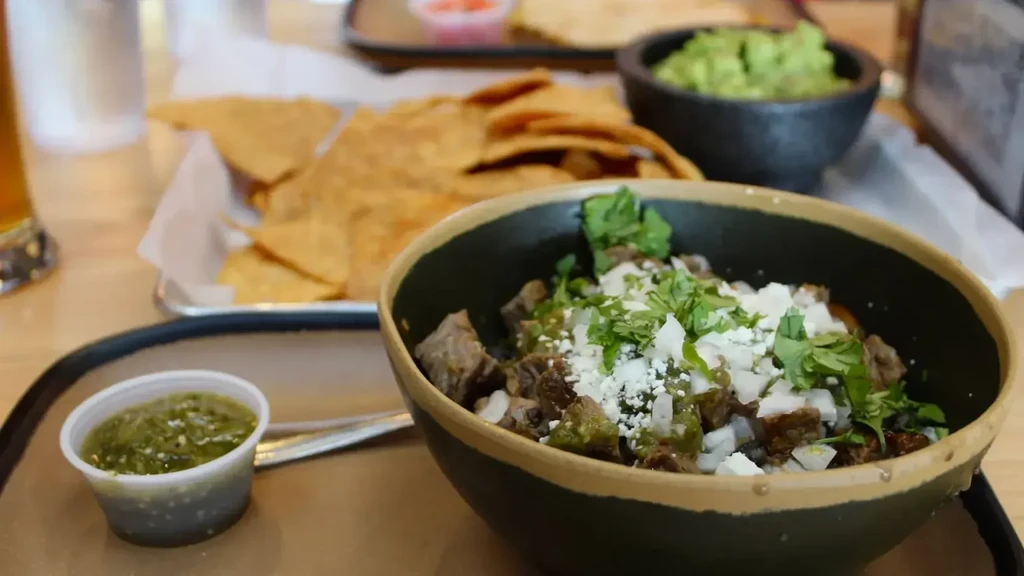 Topped meat dish with salsa verde, tortilla chips, and guacamole.