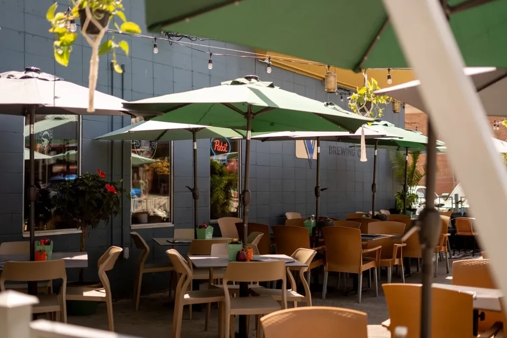 Sunny outdoor beer garden with empty tables, green umbrellas, and Pabst sign.