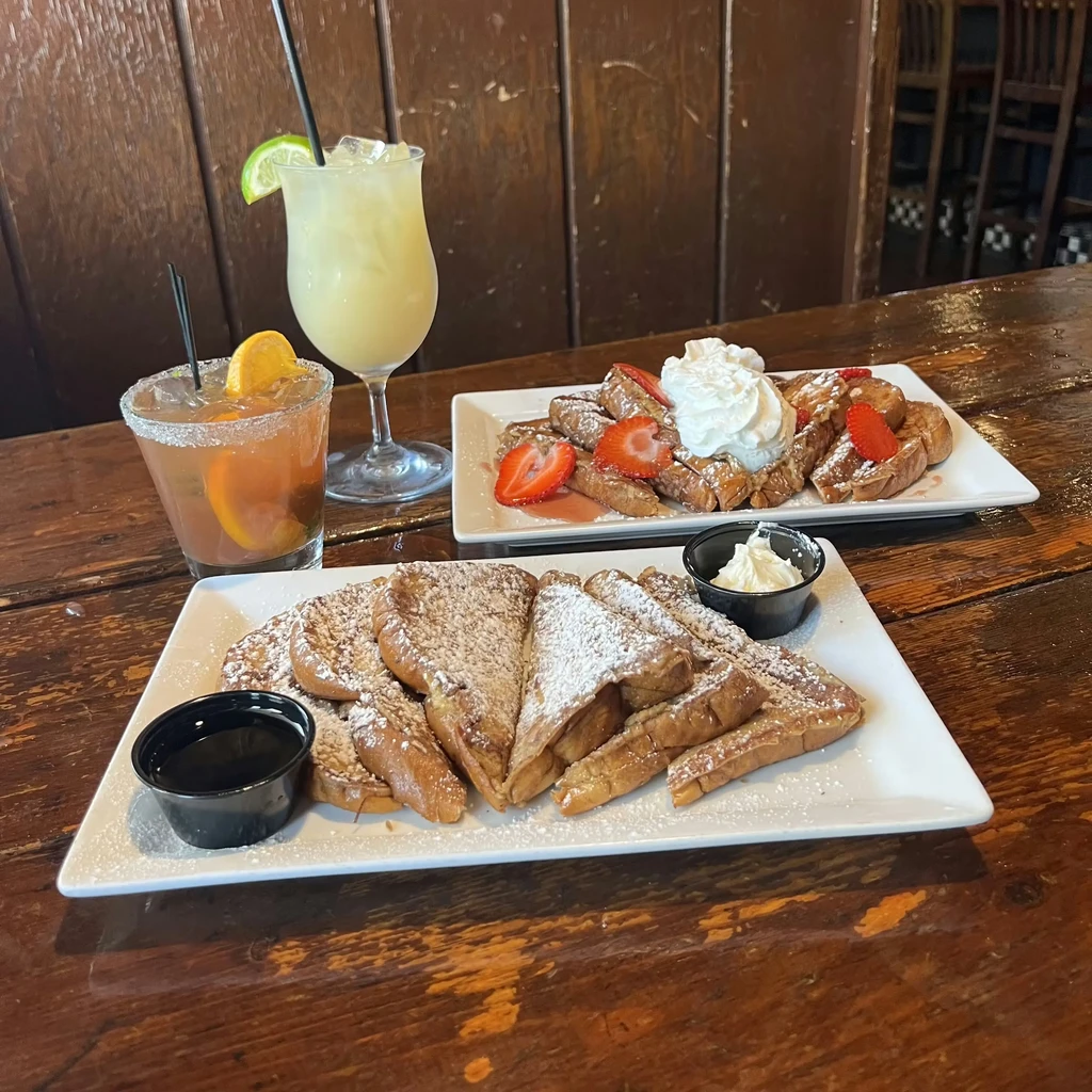 Two French toast plates with fruit, whipped cream, and two cocktails.