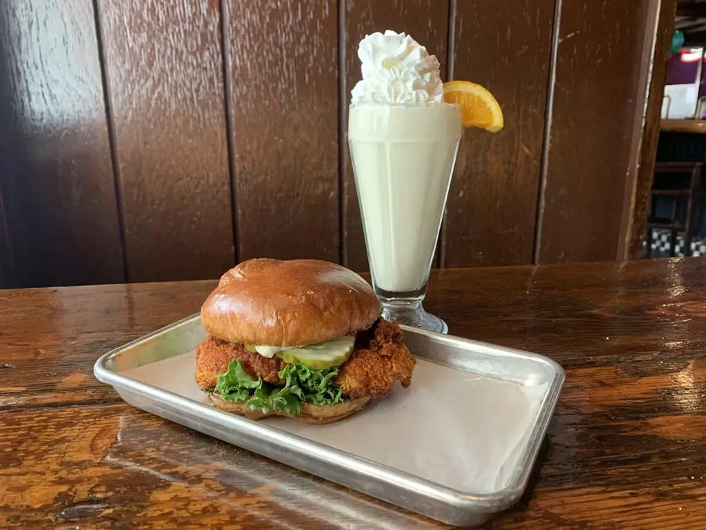 Crispy fried chicken sandwich and a milkshake with whipped cream, orange.