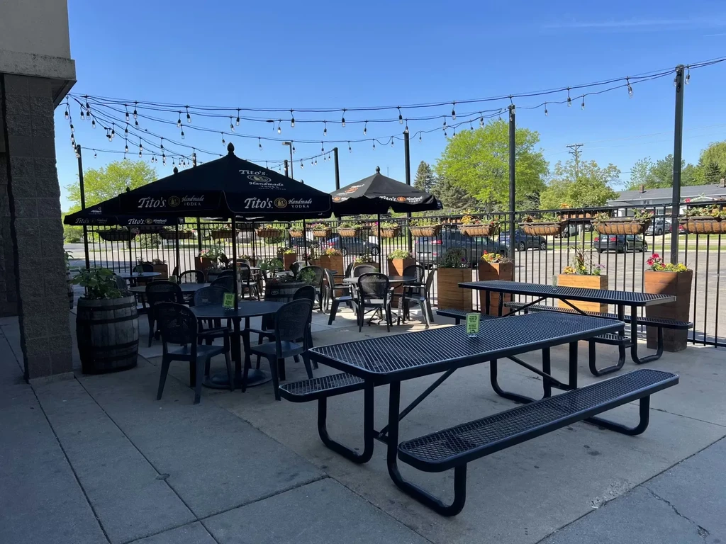 Outdoor patio with black tables, chairs, Tito's umbrellas, and string lights.