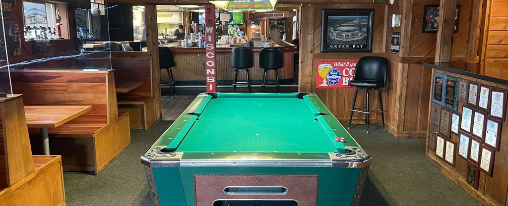 Green felt pool table inside a wood-paneled bar with Wisconsin decor.