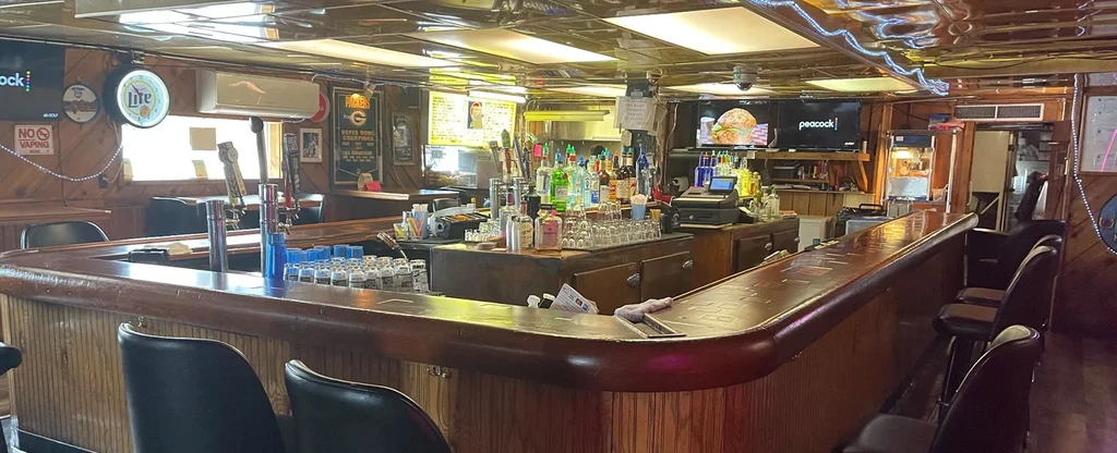 U-shaped wooden bar interior, stocked bottles, TV, and sports decor.