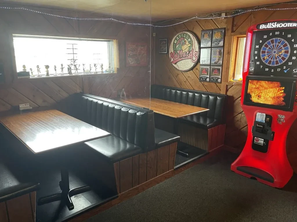 Wood-paneled pub interior with black booths and a red dartboard.