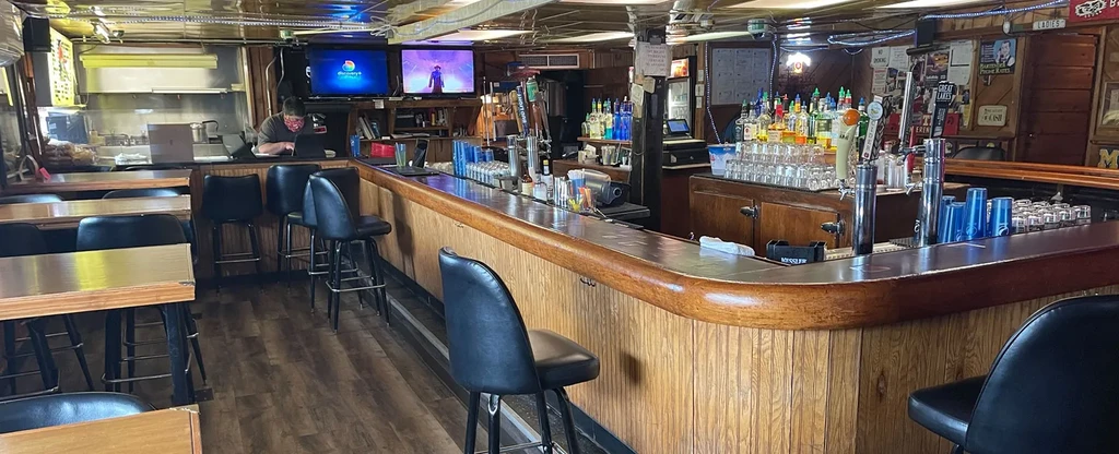 Casual bar interior with a long curved wooden counter and stools.