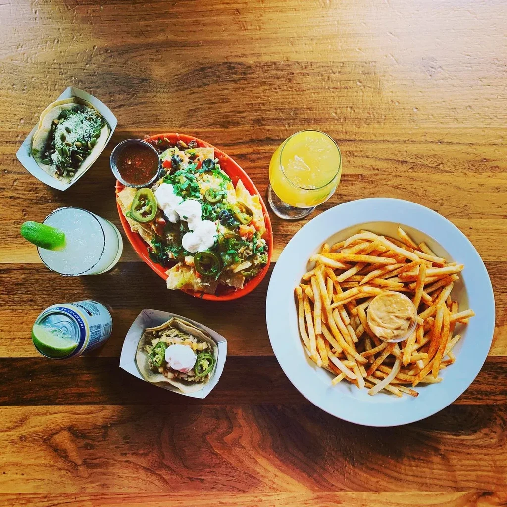 Overhead view of a rustic table with nachos, fries, tacos, and drinks.