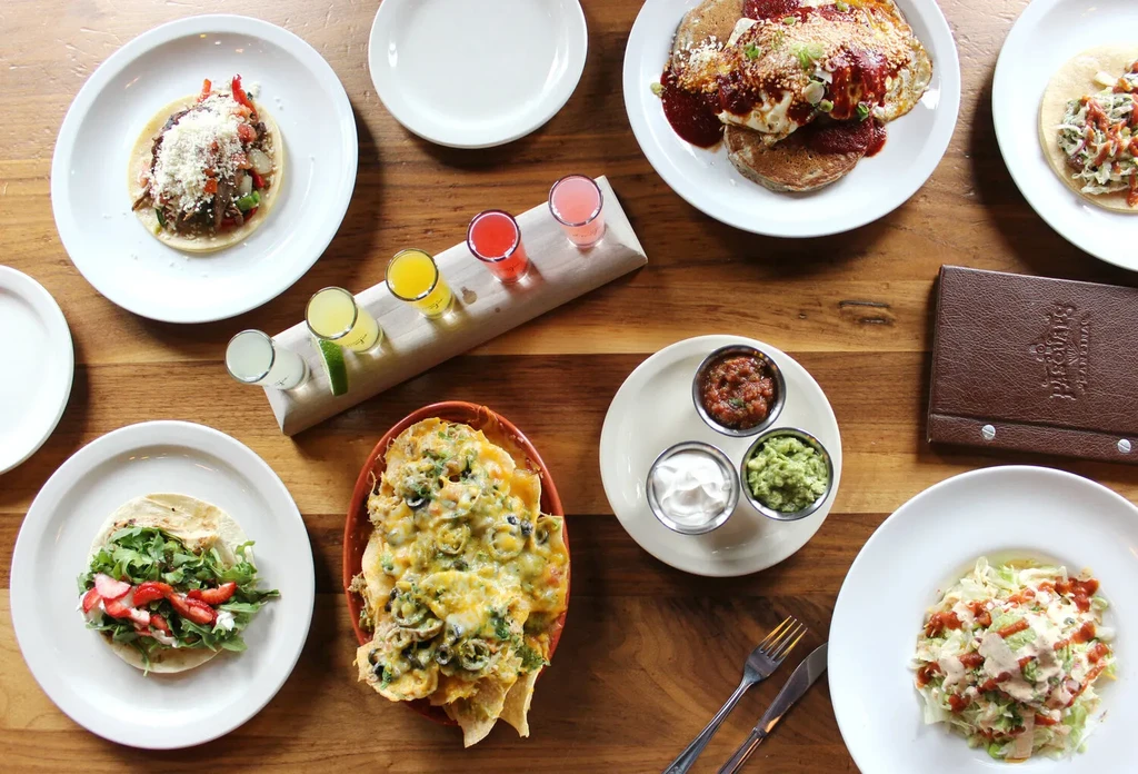 Overhead table with diverse Mexican food, tacos, nachos, and colorful drinks.