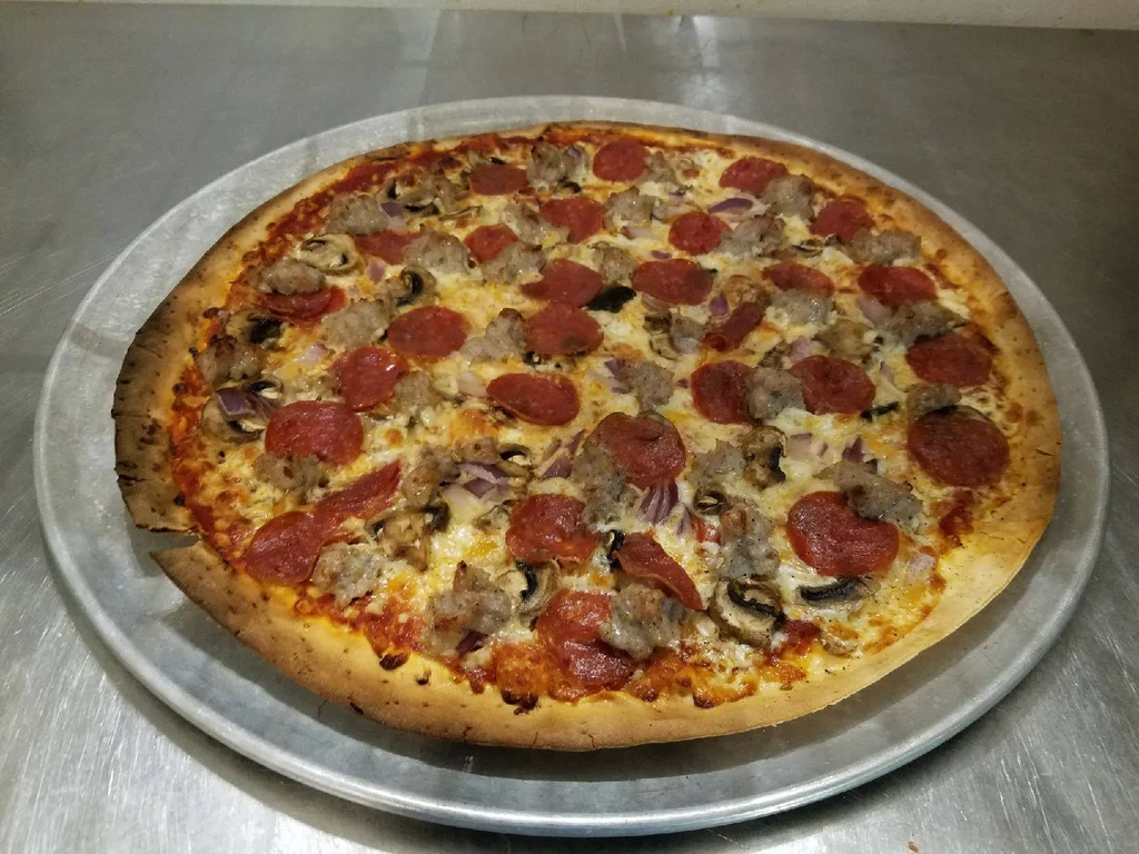 Baked pizza with pepperoni, sausage, mushrooms, and onions on metal pan.