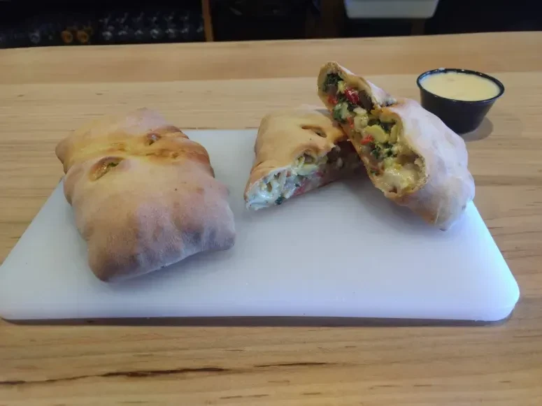 Two breakfast pastries with egg, meat, and vegetable filling and sauce.
