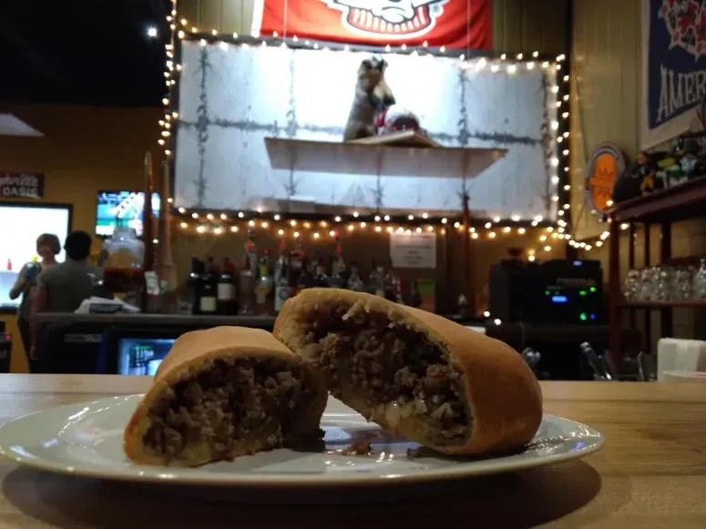 Savory pastry cut in half with meat and vegetable filling, on a plate.