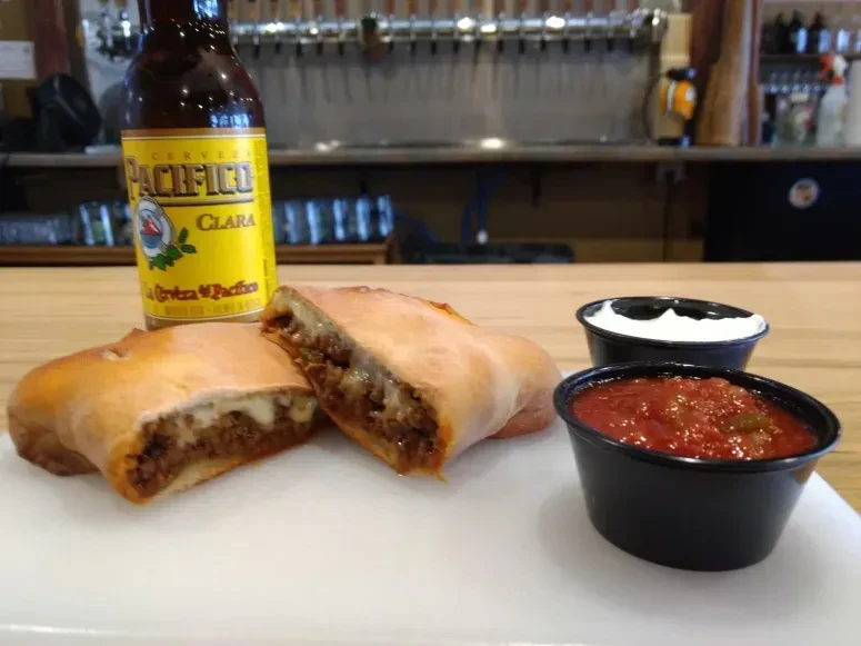 Cut savory pastry, salsa, sour cream, and Pacifico beer, bar setting.