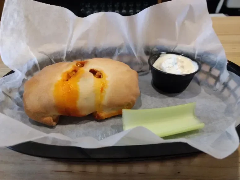 Savory pastry oozing orange filling with dip and celery in basket.