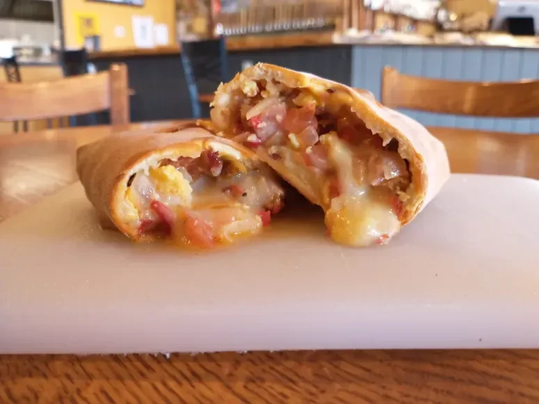 Savory pastry cut open, showing melted cheese, eggs, and red ingredients.