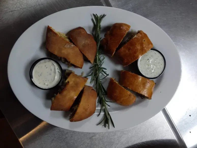 Golden-brown pastry segments with dark filling, rosemary, and dipping sauces.