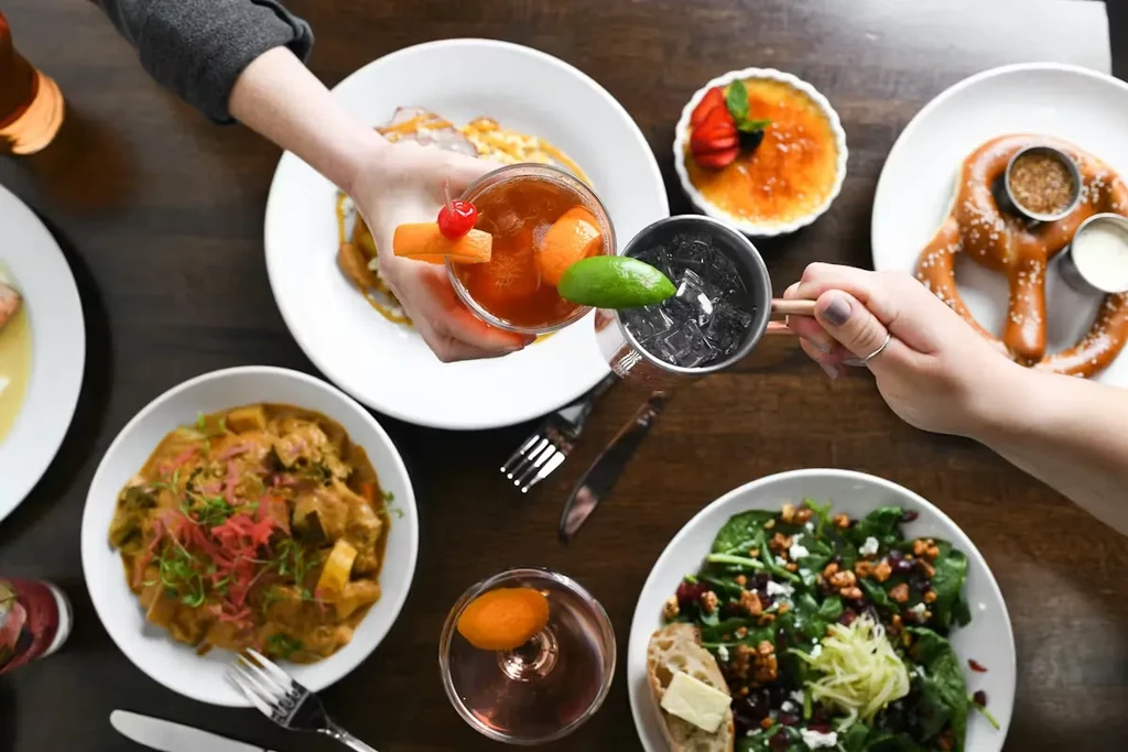 Overhead view of diverse food and drinks with hands toasting.