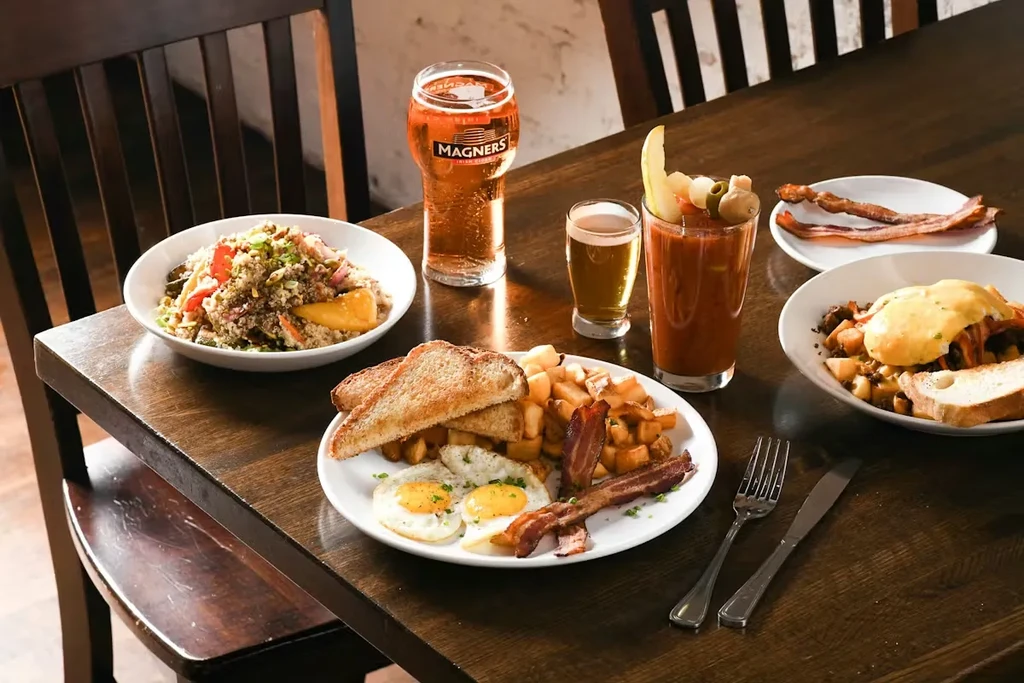 Assortment of breakfast dishes: fried eggs, bacon, eggs benedict, quinoa, and drinks.