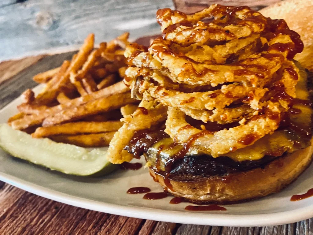 Close-up of a burger with onion rings, fries, and a pickle spear.