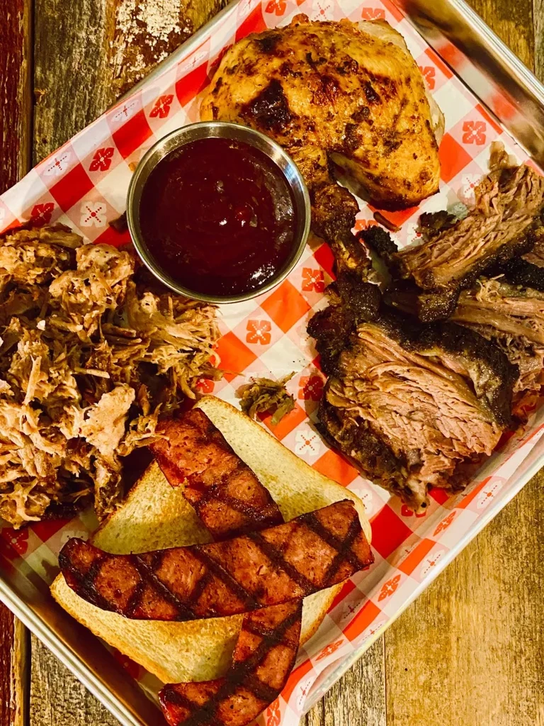 Tray of BBQ pulled pork, chicken quarter, sausage, bread, and sauce.
