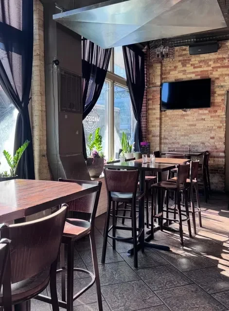 Empty modern bar with high-top tables, exposed brick, and large windows.
