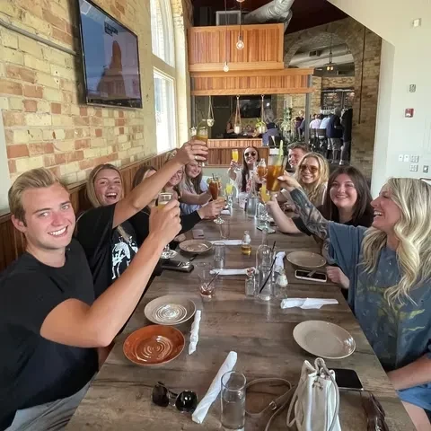 People toasting drinks at a long wooden restaurant table.