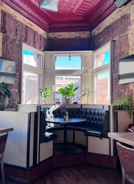 Restaurant booth with black leather, stone, ornate purple ceiling, city view.
