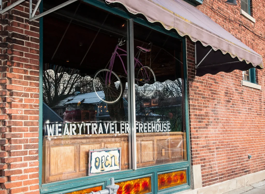 "WEARY TRAVELER FREEHOUSE" brick storefront displays purple bicycle, "OPEN" sign.