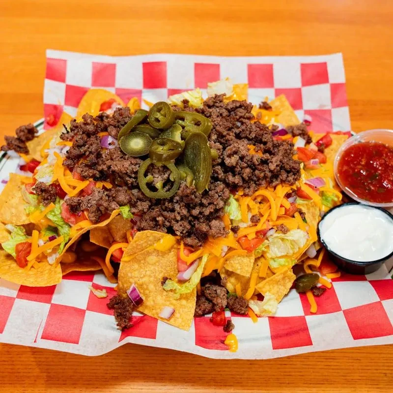 Large nachos with beef, cheese, jalapeños, lettuce, and side dips.