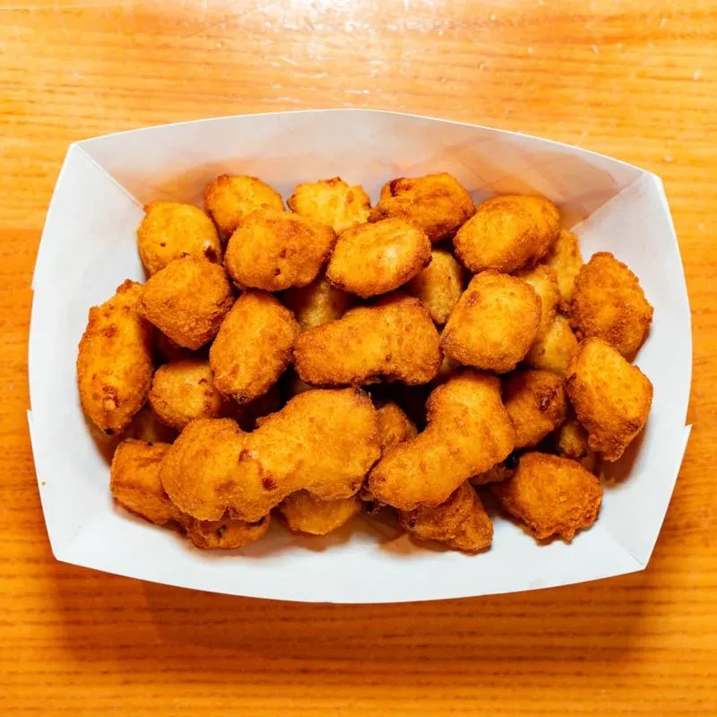 Golden-brown, crispy fried cheese curds piled in a white paper tray.