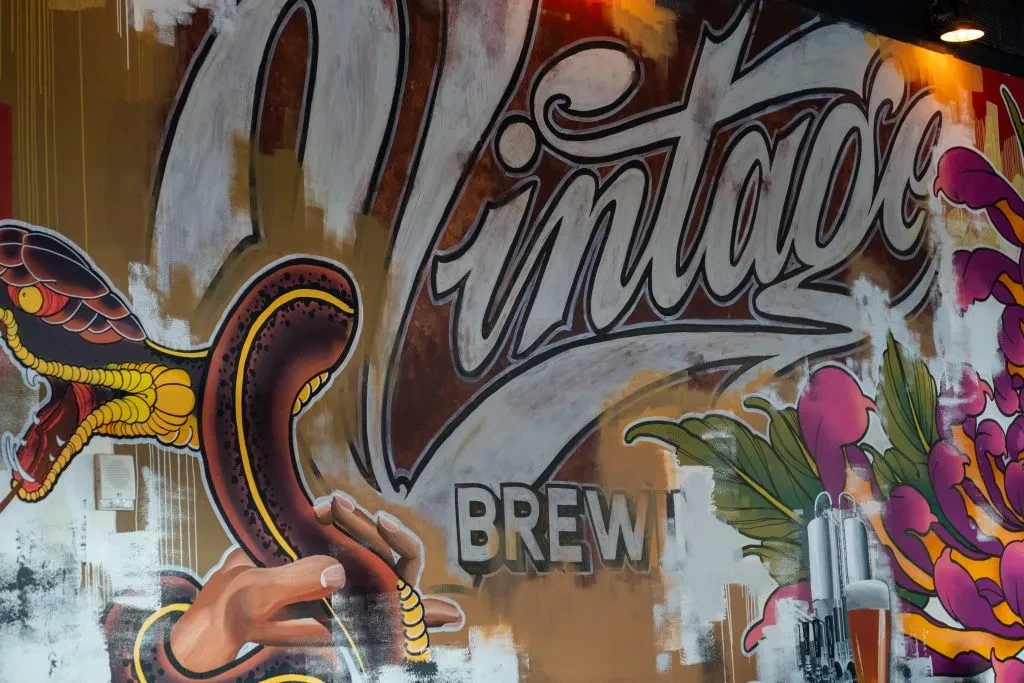 Mural of a snake, human hand, brewery tanks, and 'Vintage BREW'.