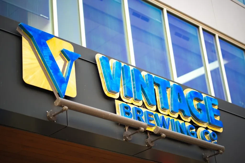Blue and yellow 3D VINTAGE BREWING CO. sign on a dark building.