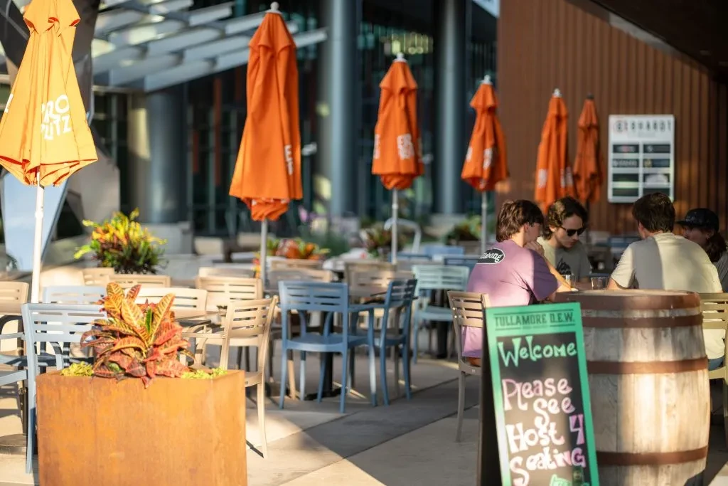 Sunny outdoor restaurant patio with orange umbrellas and diners.
