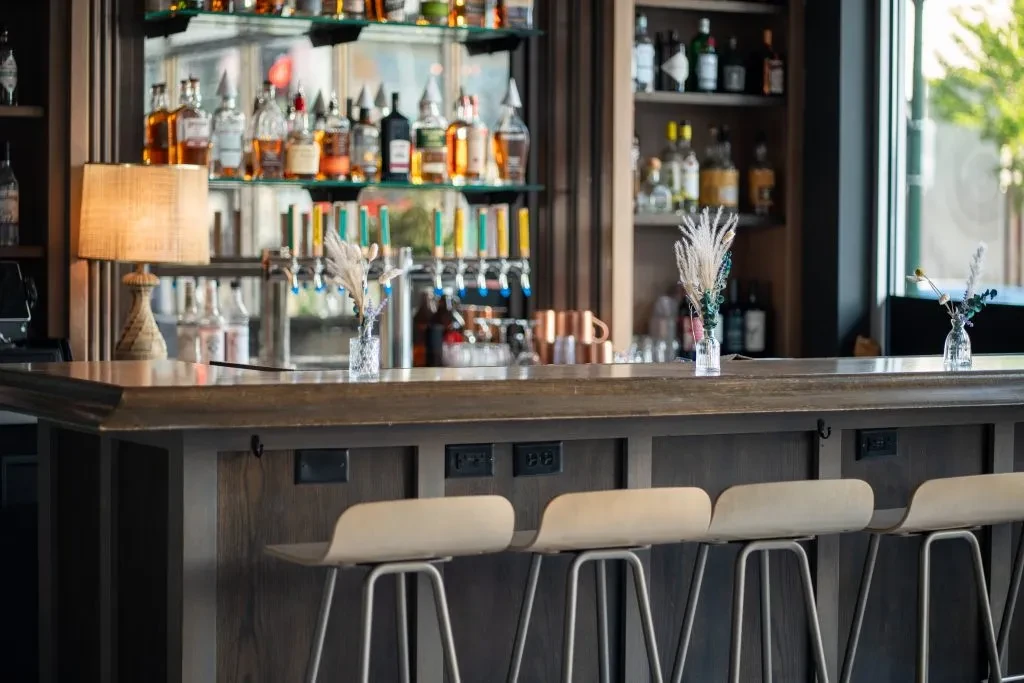 Modern bar with wooden counter, stools, liquor bottles, and beer taps.