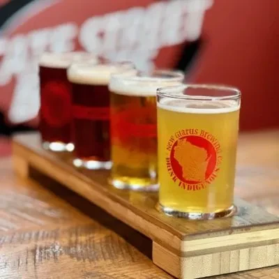 New Glarus beer flight with five diverse beers on a wooden paddle.