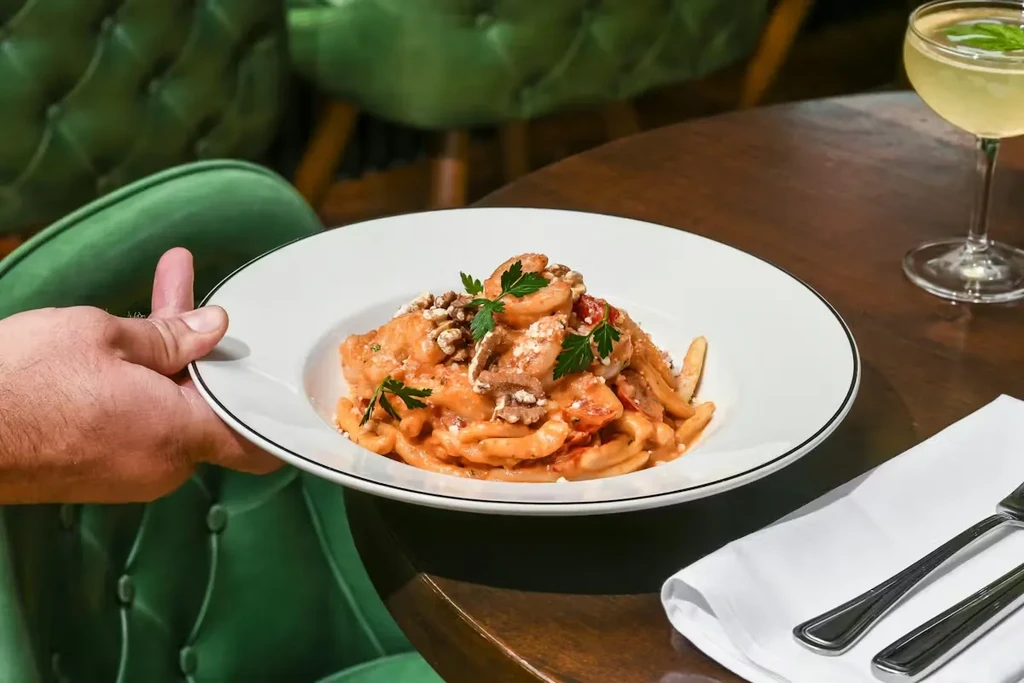 Restaurant table with shrimp pasta, cocktail, and green chairs.