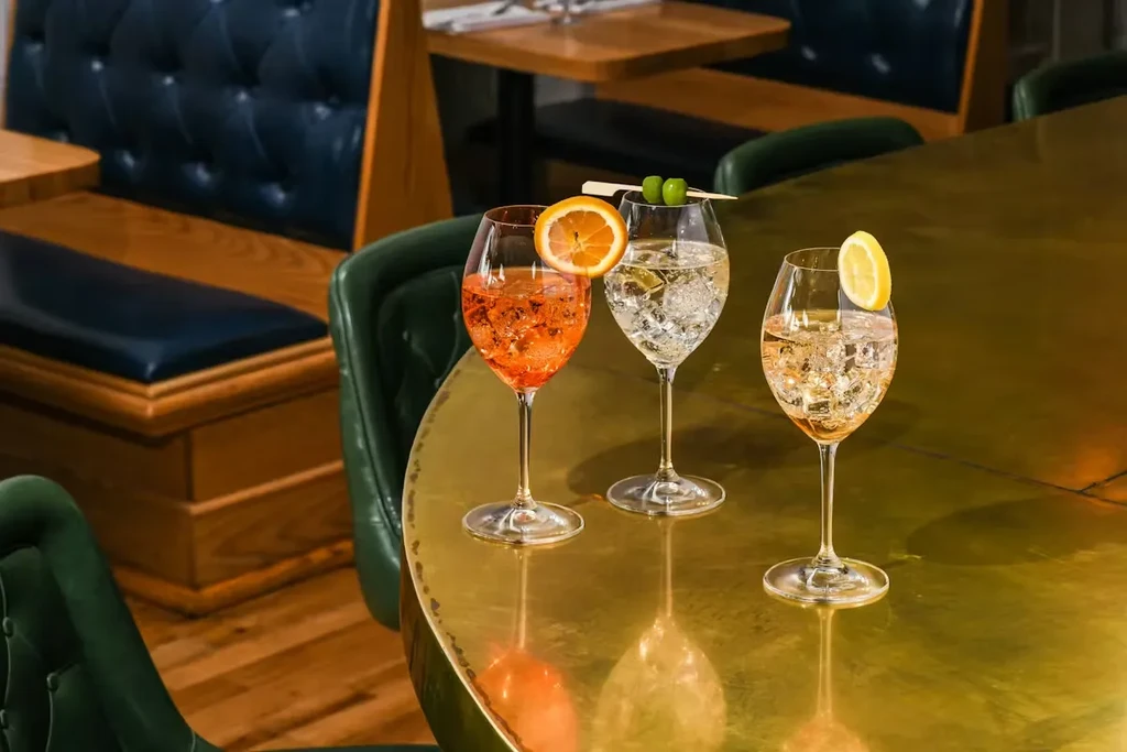 Orange, olive, and lemon garnished cocktails on a golden table.