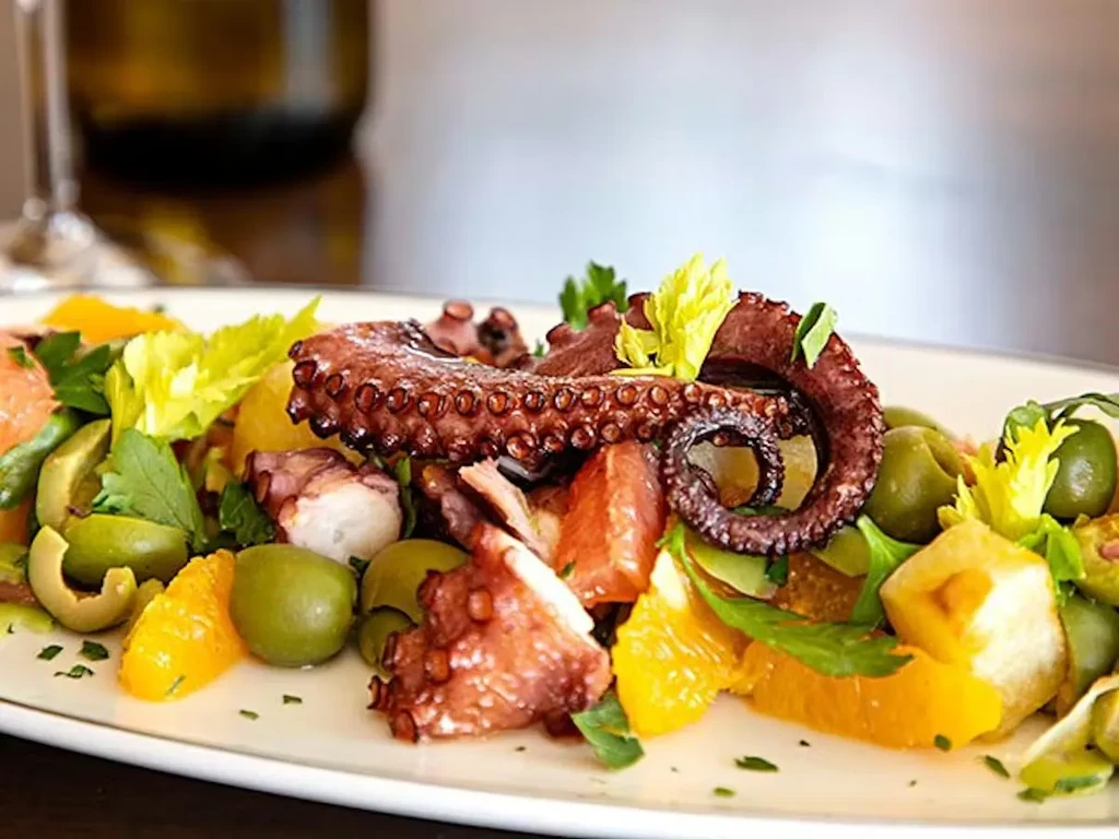 Well-plated octopus salad with olives, orange, and celery.