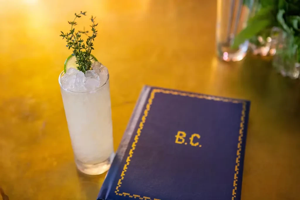 Cocktail with lime and herb, blue book with 'B.C.' on gold.