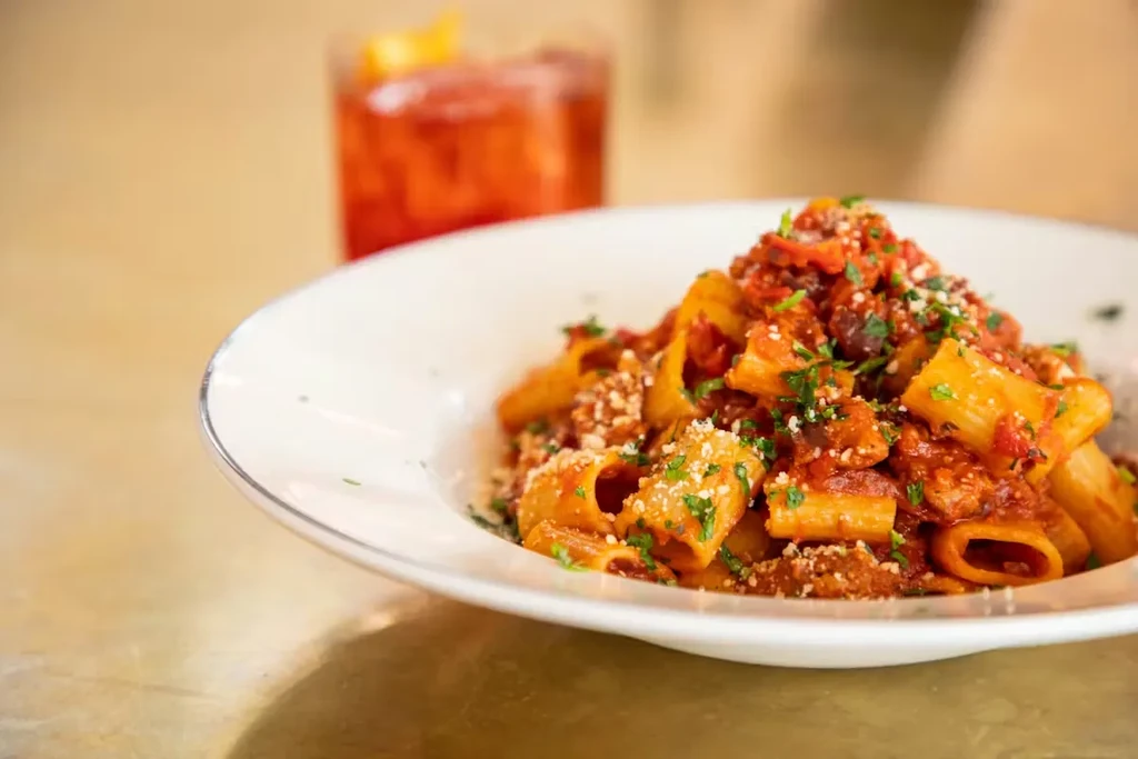 Pasta with chunky red sauce, grated cheese, green herbs, blurred drink.