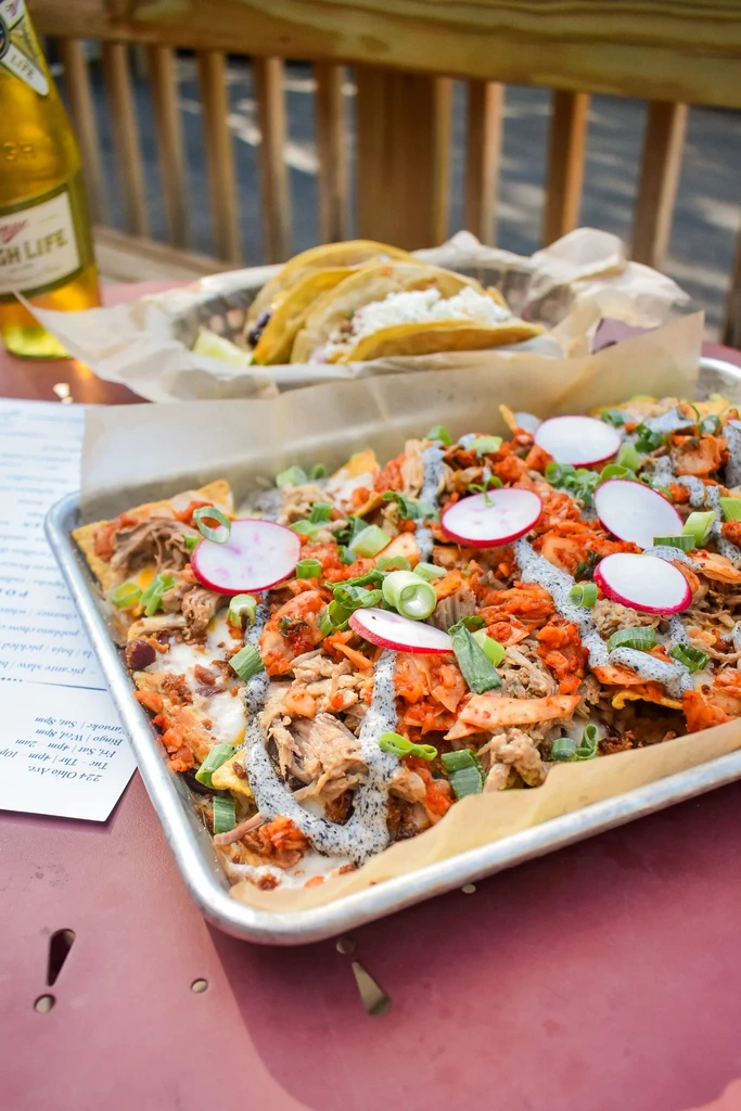 Nachos with meat, kimchi, radishes, tacos, and beer on an outdoor patio.