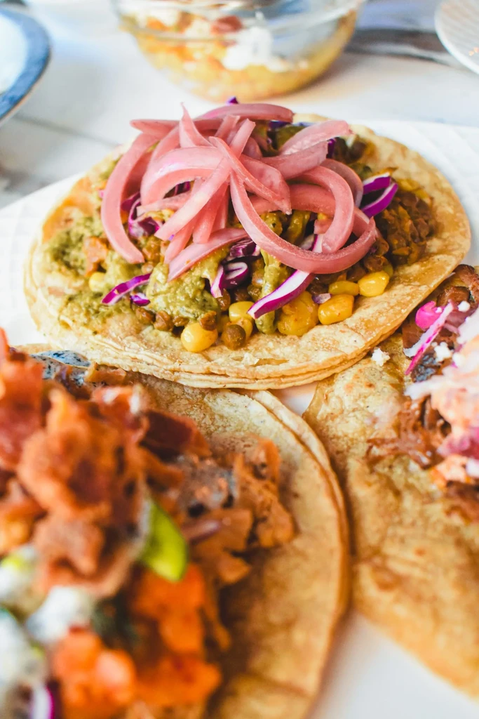 Tacos on a white plate, one with purple cabbage and pink pickled onions.