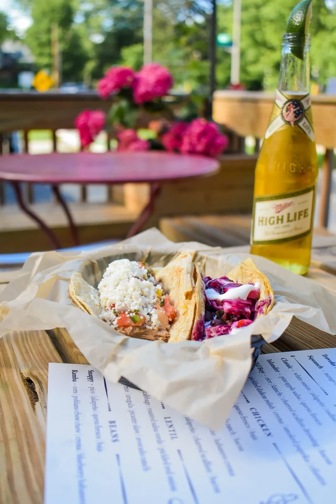 Two tacos, Miller High Life beer with lime on a rustic outdoor table.