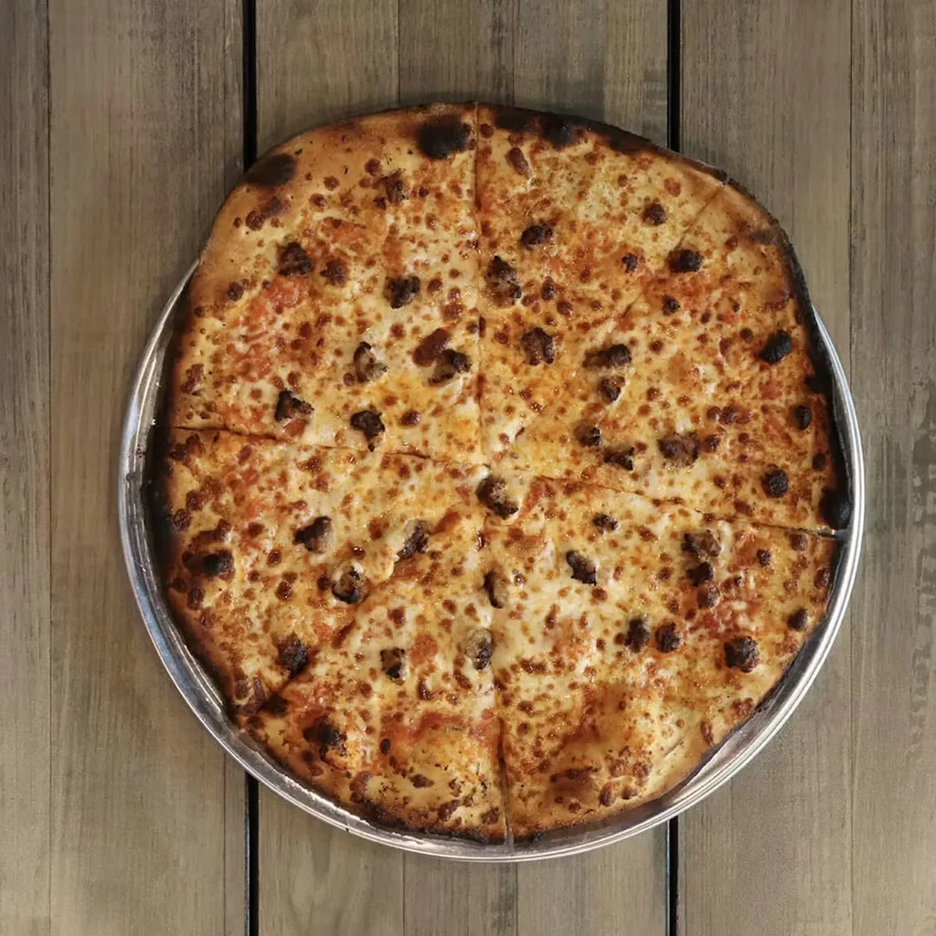 Sliced pizza with bubbly cheese and dark meat on a wooden table.
