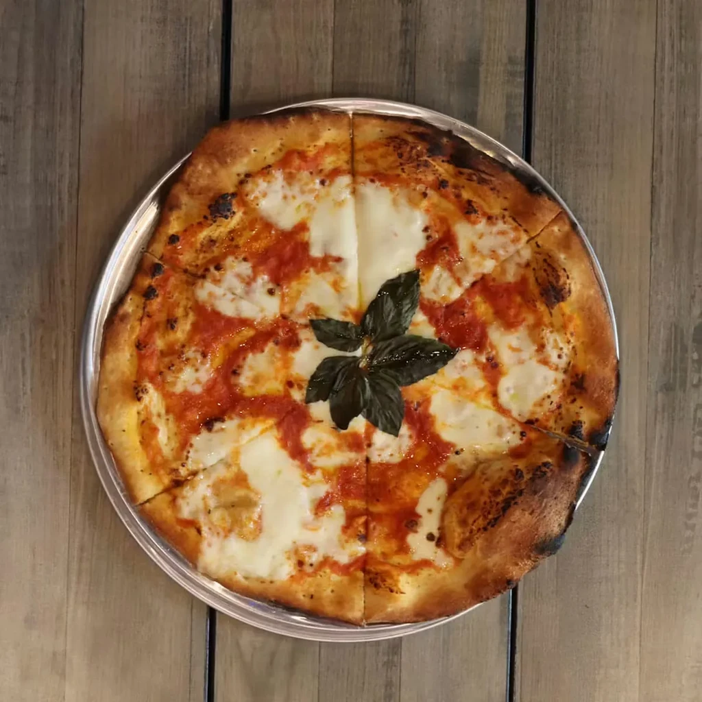 Freshly baked Margherita pizza, sliced, on a rustic wooden table.